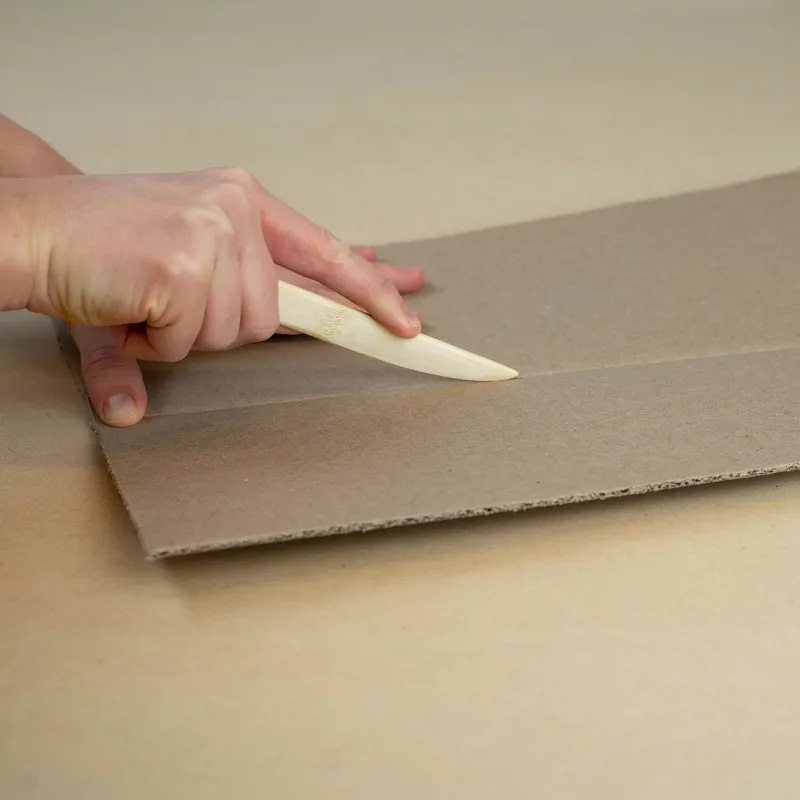 Scoring tool creasing a cardboard sheet