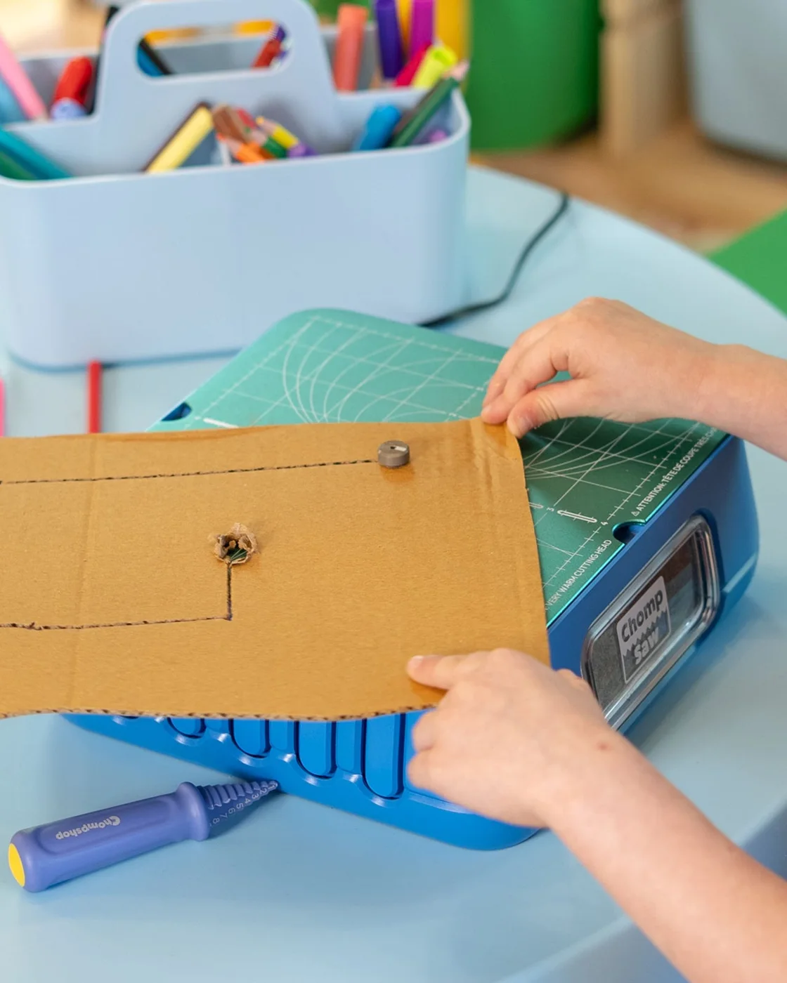 Hands guiding a cardboard sheet through the ChompSaw