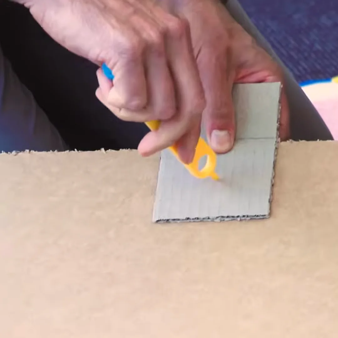 A hand punching a hole in cardboard with a Makedo Mini-Tool